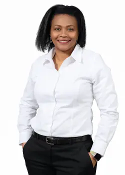 Smiling woman in a white blouse and black trousers, hands in pockets, posing in a professional portrait.